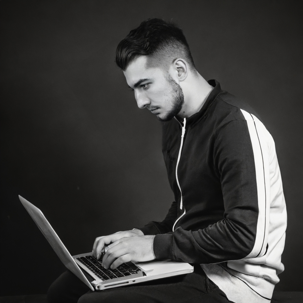 Homme tapant sur son ordinateur. Cet homme représente les designers qui travailleront sur différents projets artistiques. La photo est en noir et blanc